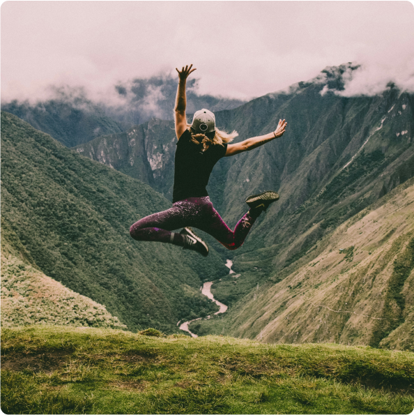 Frau springt vor Freude vor einer Berglandschaft.